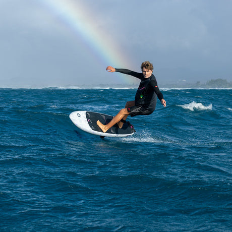 Person surf foiling on a wave with Duotone Paradox foil board rainbow in the background