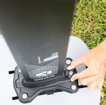 Person adjusting a Duotone Quick Mount Mast on a Duotone wingfoil board with grass in the background